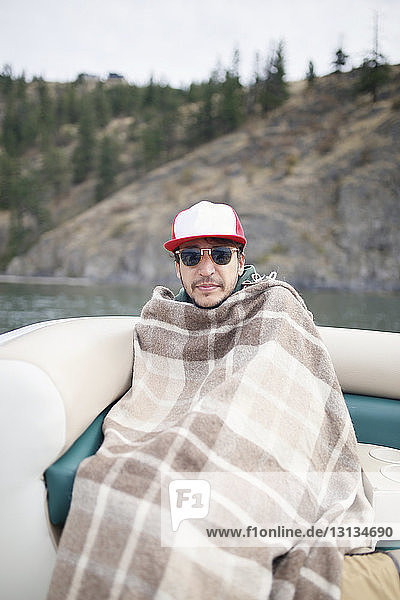 Portrait of man wrapped in blanket sitting on boat against mountain