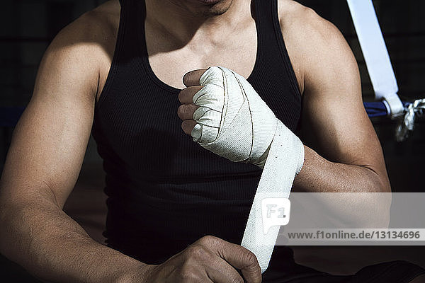Midsection of sportsman wrapping bandage on hand in gym