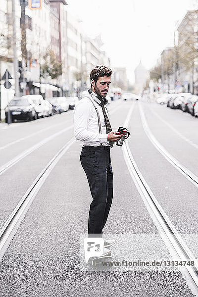 Geschäftsmann in voller Länge beim Telefonieren während des Skateboardfahrens auf der Straße in der Stadt