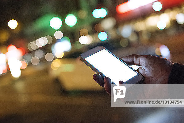 Cropped hand holding smart phone in illuminated city at night