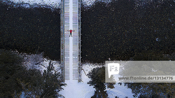 Mid distance view of hiker lying on footbridge in forest during winter