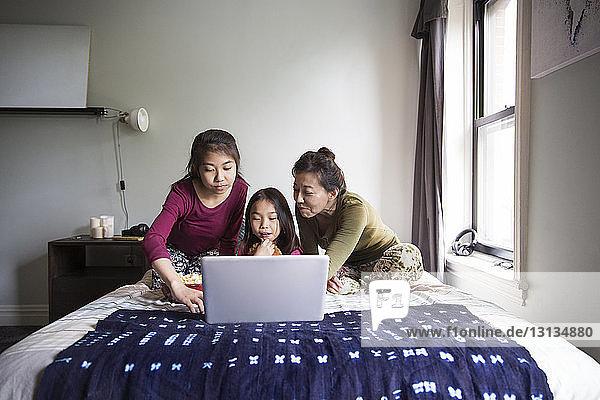 Familie schaut zu Hause auf den Laptop im Bett