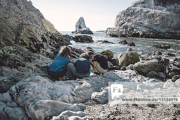 Friends playing while crouching on rocks at beach