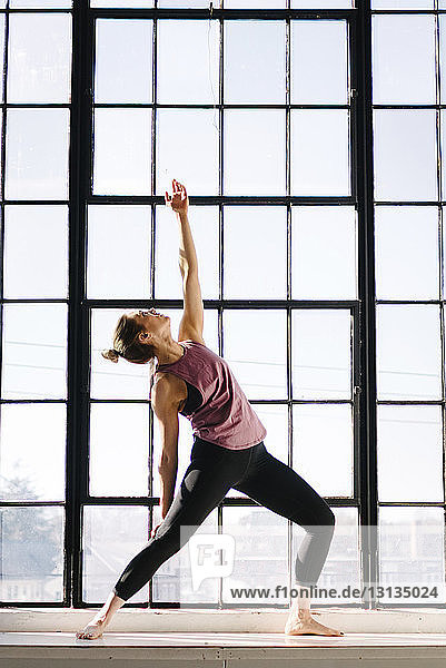 Female athlete practicing yoga by window in gym