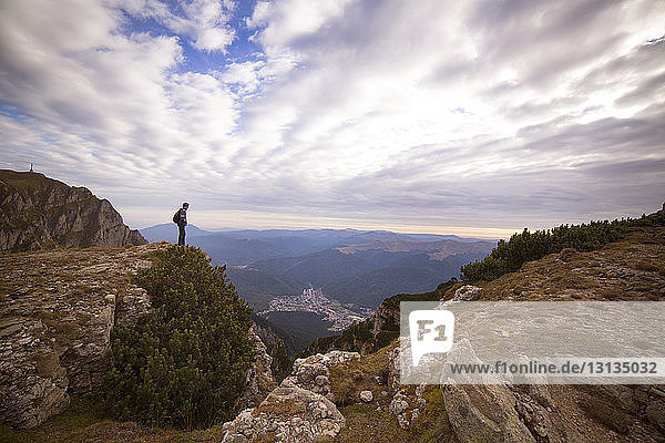 Side view of man standing on mountain against cloudy sky