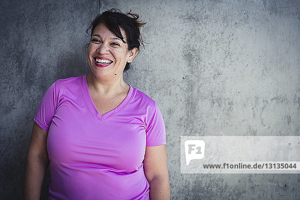 Portrait of cheerful woman standing against wall in yoga studio