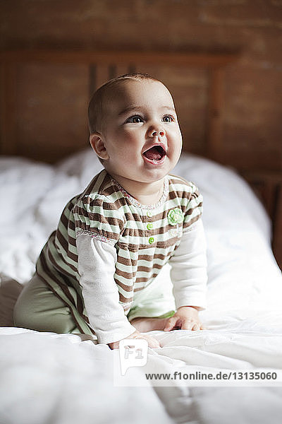 Süßes Baby-Mädchen schaut auf  während es zu Hause auf dem Bett kniet