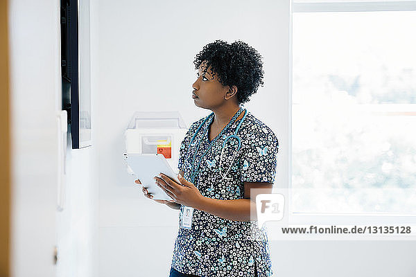 Ärztin schaut auf Flachbildschirm  während sie im Krankenhaus einen Tablet-Computer in der Hand hält
