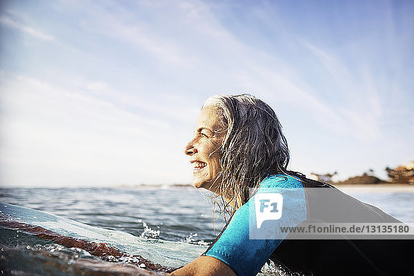 Side view of happy mature woman lying on surfboard in sea