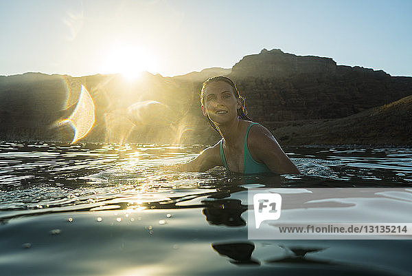 Woman swimming in sea against mountain during sunset
