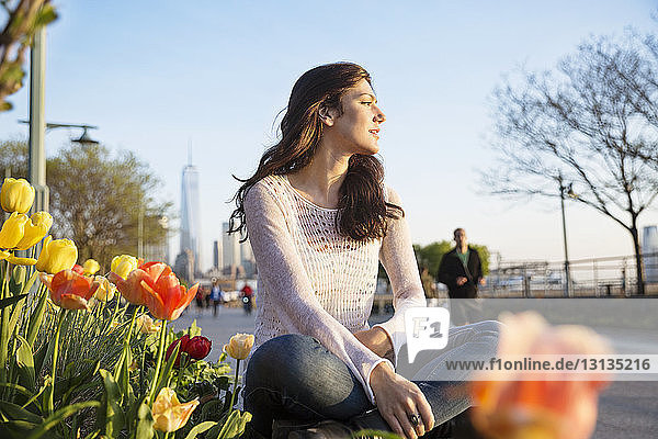 Nachdenkliche Frau sitzt auf einer Stützmauer mit dem One World Trade Center im Hintergrund