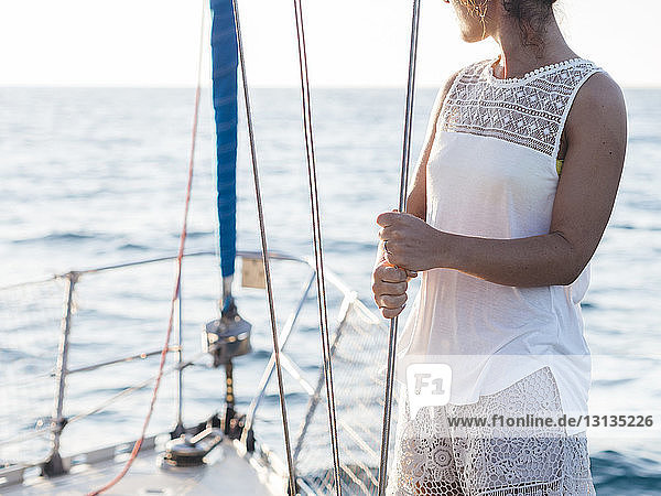 Mittelteil einer mittelgroßen erwachsenen Frau  die ein Seil hält  während sie im Segelboot auf See steht