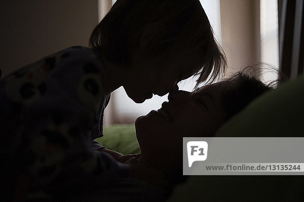 Scherenschnitt Mutter und Tochter reiben sich beim Entspannen zu Hause im Bett