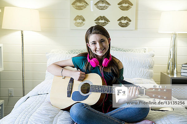 Portrait of happy teenage girl playing guitar in bedroom
