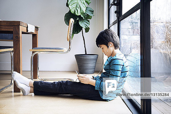 Junge benutzt digitales Tablett  während er am Fenster sitzt