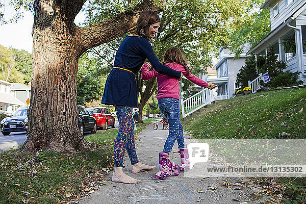 Mother assisting daughter in skating on footpath during autumn
