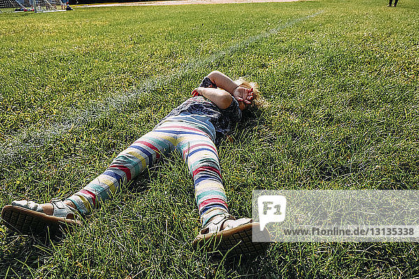 Hochwinkelaufnahme eines sorglosen Mädchens  das auf einem Rasenfeld auf einem Spielplatz liegt