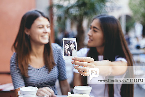 Frau zeigt Sofortfoto  während sie mit einem Freund im Straßencafé sitzt