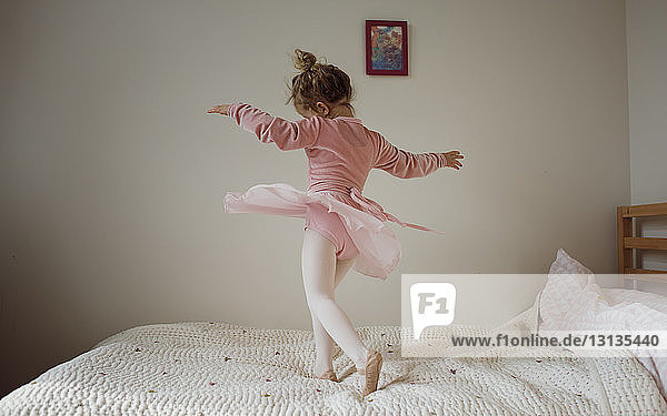 Girl in ballet costume dancing on bed at home