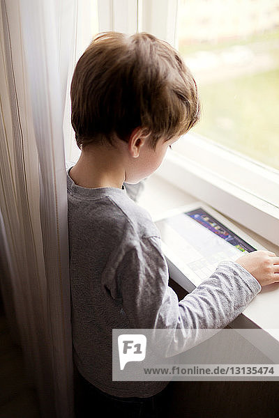 Hochwinkelansicht eines Jungen am Tablet-Computer  während er zu Hause am Fenster steht
