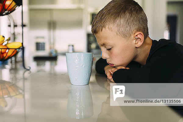 Seitenansicht eines müden Jungen mit einer Teetasse  der mit dem Kopf auf dem Küchentisch zu Hause liegt