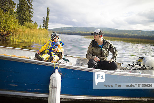 Father and son sitting in boat on lake
