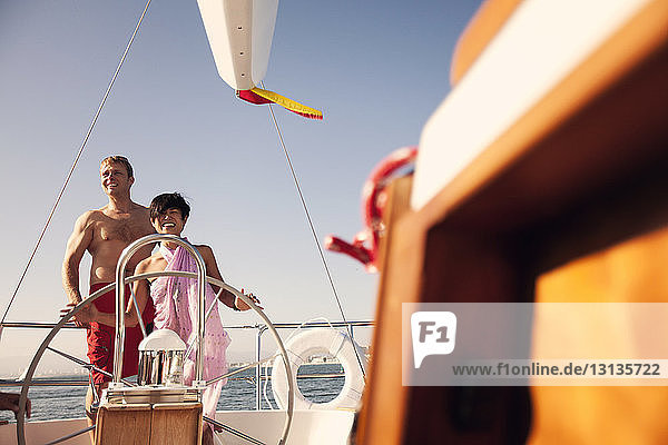 Smiling couple standing by steering wheel on boat at sea