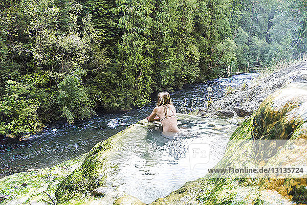 Rear view of woman swimming in hot spring by stream at forest