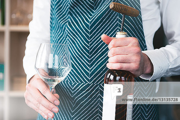 Midsection of bartender holding wineglass with bottle while standing in tasting room