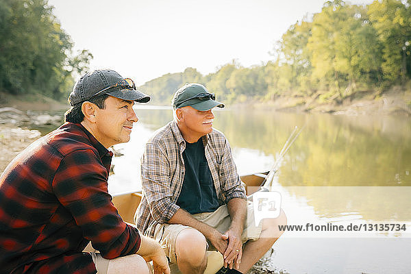 Male friends looking away while sitting on boat at lakeshore