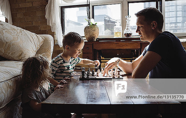 Seitenansicht eines Vaters  der zu Hause mit Kindern auf dem Tisch Schach spielt