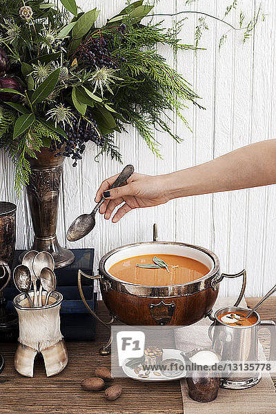 Frauenhand hält Löffel über Kürbissuppe auf dem Tisch