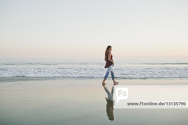 Full length of woman walking on shore against sea and clear sky during sunset