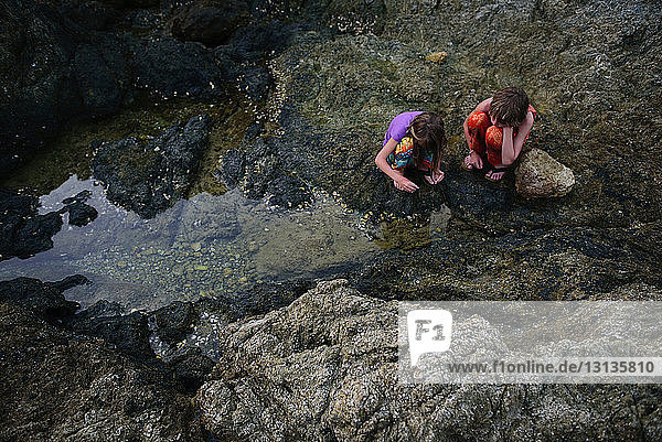 High angle view of siblings crouching on rocks at shore