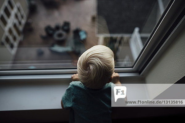 Rückansicht eines zu Hause stehenden kleinen Jungen  der durch ein Fenster schaut