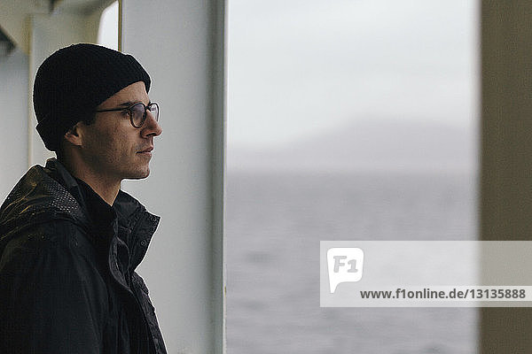 Nachdenklicher Mann schaut weg  während er im Kreuzfahrtschiff steht