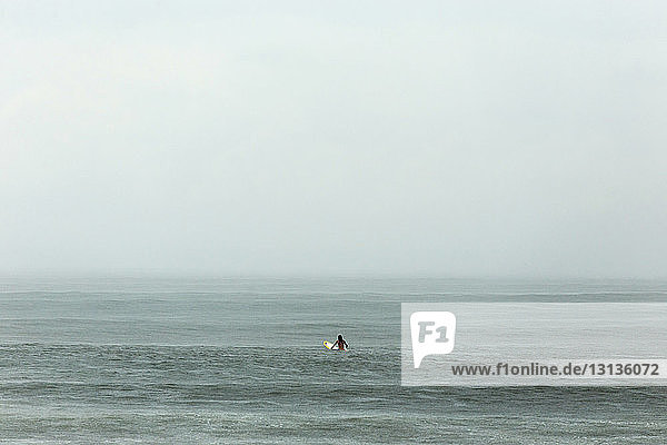 Man with surfboard in sea against sky during foggy weather