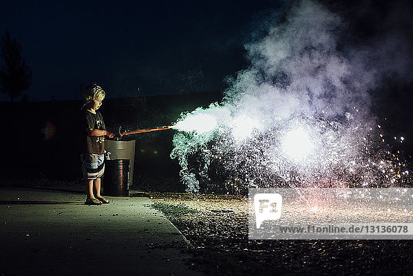 Seitenansicht eines nachts auf der Straße stehenden Jungen  der Feuerwerkskörper abbrennt