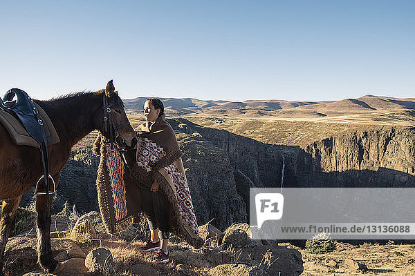 Woman stroking horse while standing on mountain against clear sky
