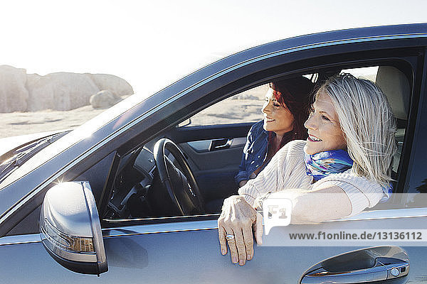 Cheerful mother and daughter looking away while sitting in car