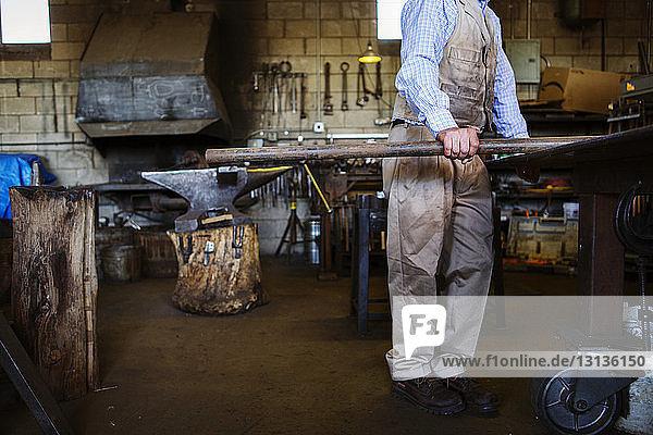 Niedriger Abschnitt eines Handwerkers  der einen Metallstab in der Fabrik hält