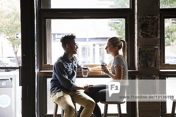 Lächelndes Paar unterhält sich  während es im Café am Fenster sitzt