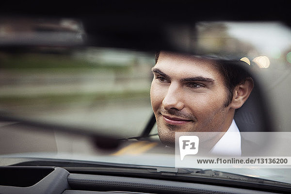 Close-up of handsome man in car reflecting on rear-view mirror