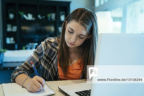 Teenage girl doing homework using laptop computer at home