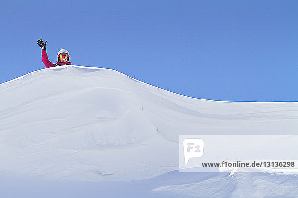 Porträt einer Frau  die auf einem schneebedeckten Berg vor klarem Himmel mit der Hand winkt