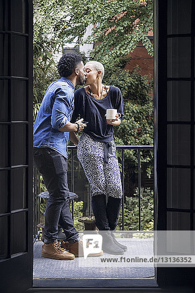 Romantisches Paar küsst sich  während es auf dem Balkon steht und durch die Tür gesehen wird