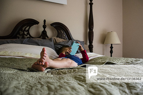 Boy using mobile phone while lying on bed at home