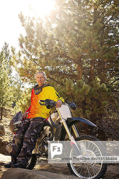 Portrait of man standing by dirt bike against trees