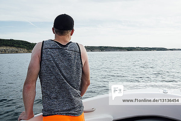 Rückansicht eines Mannes  der während einer Bootsfahrt gegen den bewölkten Himmel blickt