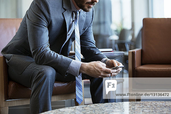 Mittelsektion eines Geschäftsmannes  der ein Smartphone auf einem Sessel im Büro benutzt